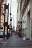 a woman walking down a sidewalk next to tall buildings