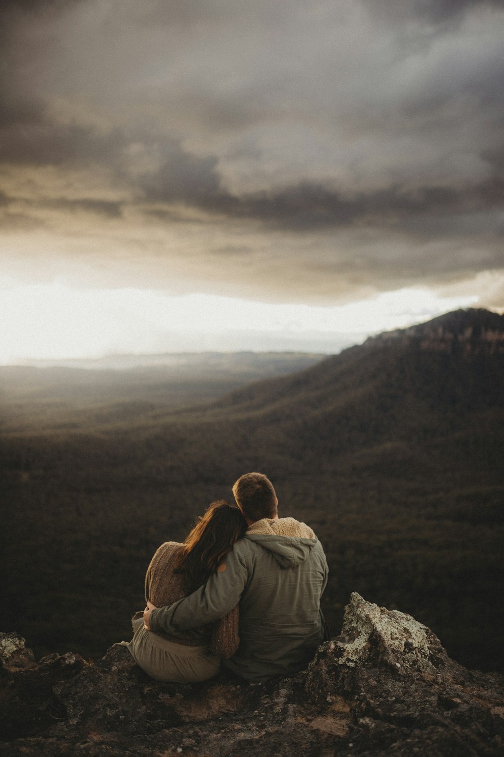 a man and woman sitting on top of a mountain