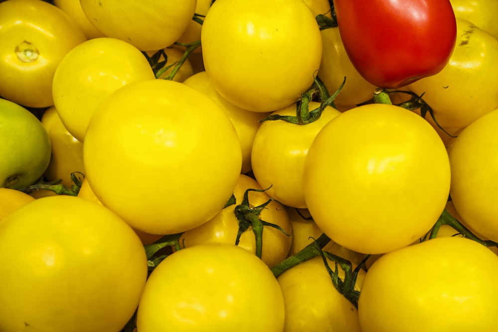 a pile of yellow tomatoes and a red pepper