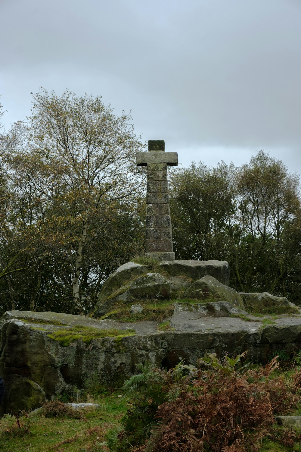 a stone cross on a hill with trees in the background