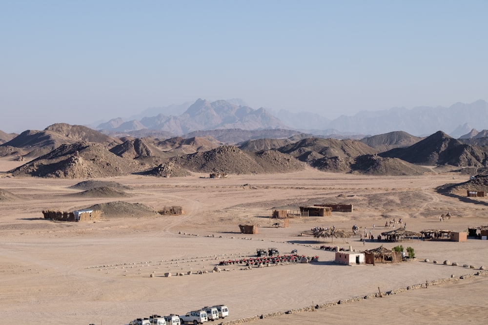 a desert with a few buildings and mountains in the background
