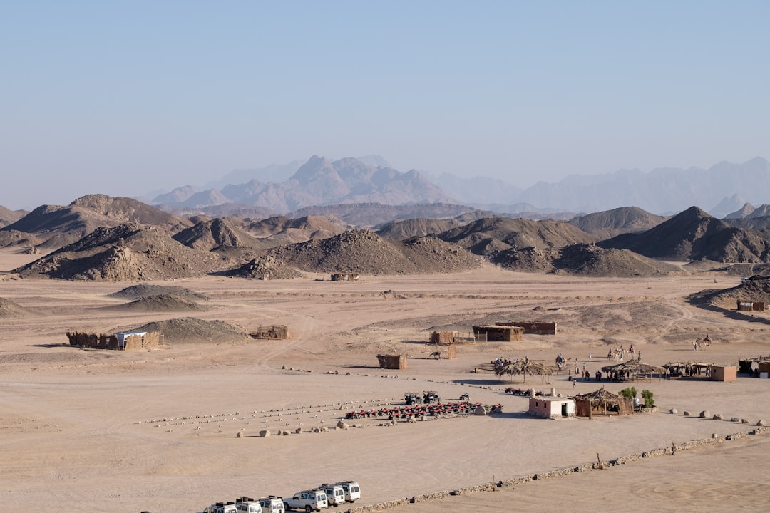 a desert with a few buildings and mountains in the background,