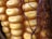 Close-up view of corn on the cob, showing its golden yellow kernels tightly packed in rows. Brown silk strands surround the corn, adding texture to the image.