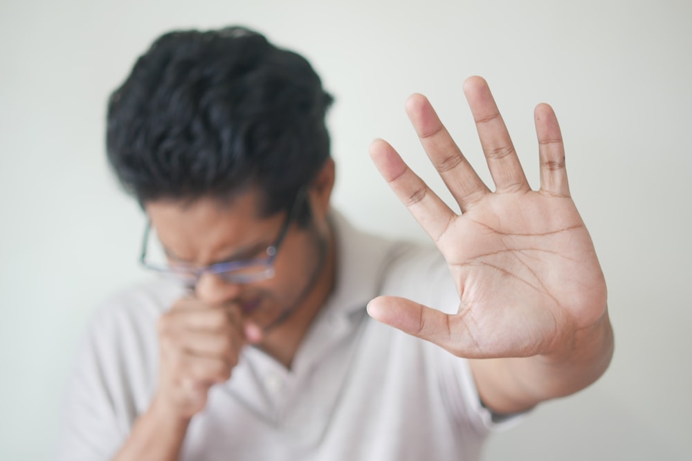 Person coughing and covering mouth in blurred background, in-focus hand in foreground. oral cancer