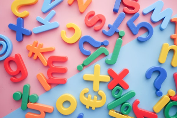 Assemblage de lettres, de chiffres et de symboles en plastique multicolore éparpillés sur un fond rose et bleu.