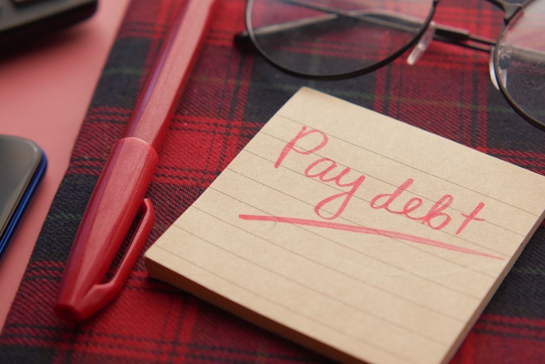 a note that says pay debt next to a pen and glasses,