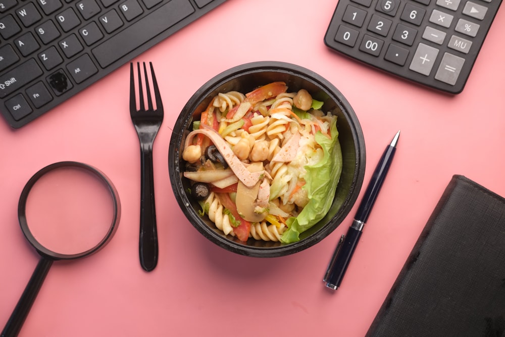 a bowl of pasta salad next to a keyboard and a pair of scissors