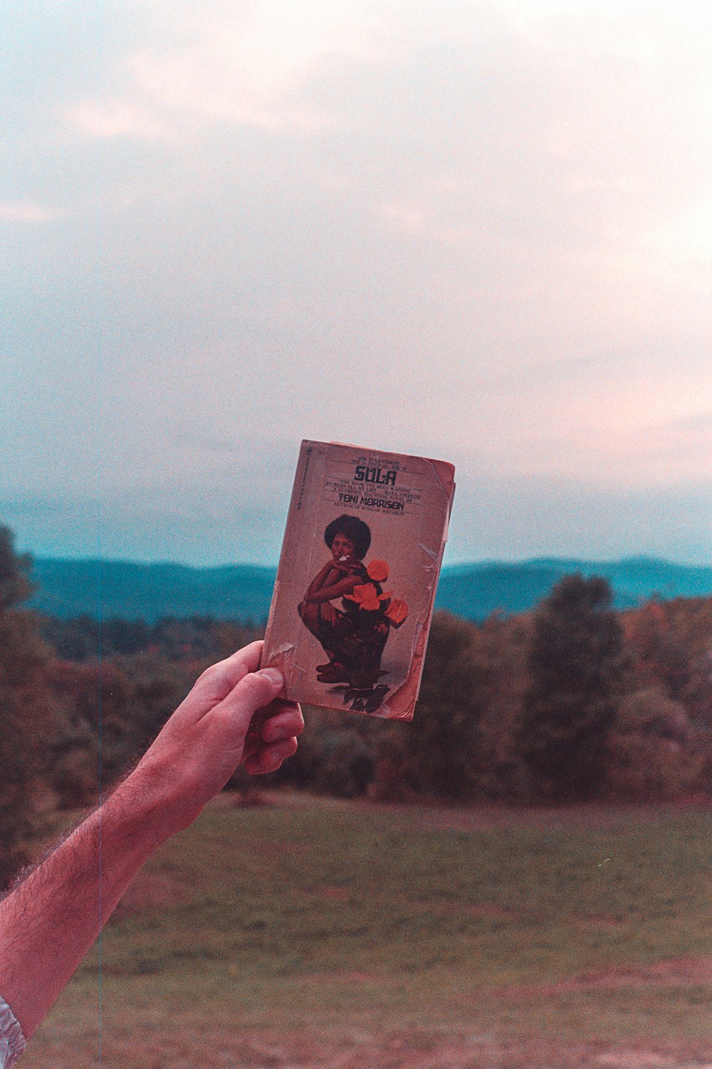 a person holding up a book in front of a field