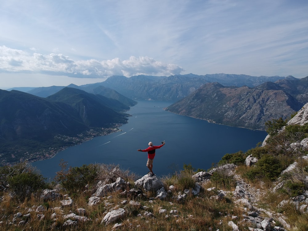 a man standing on top of a mountain next to a lake