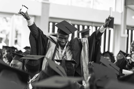 A confident graduate proudly holding a digital diploma with luxury cars in the background.