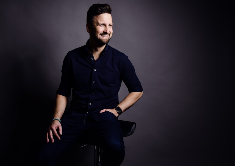 En man som sitter på en barstol med sin hand i ena fickan och den andra handen på vänster sida lår