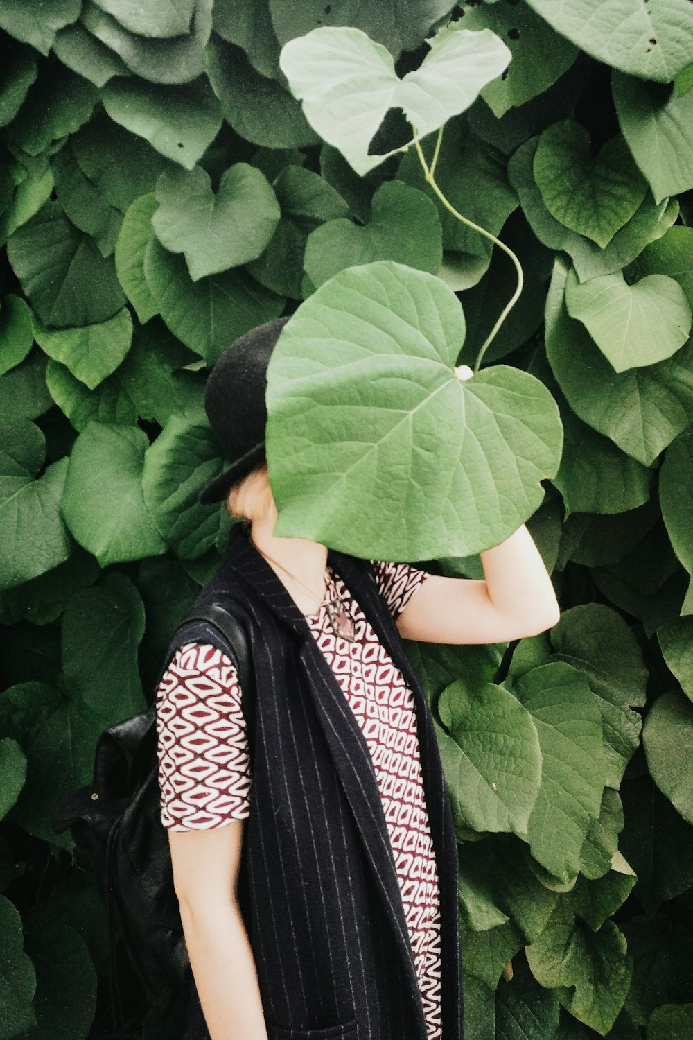 a person standing in front of a bush with a large leaf