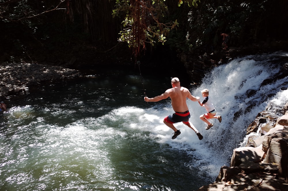 Un hombre y dos niños saltando de una cascada