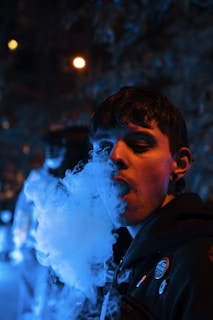 Person vaping outdoors at night with blurred city lights and neon signs creating a futuristic vibe