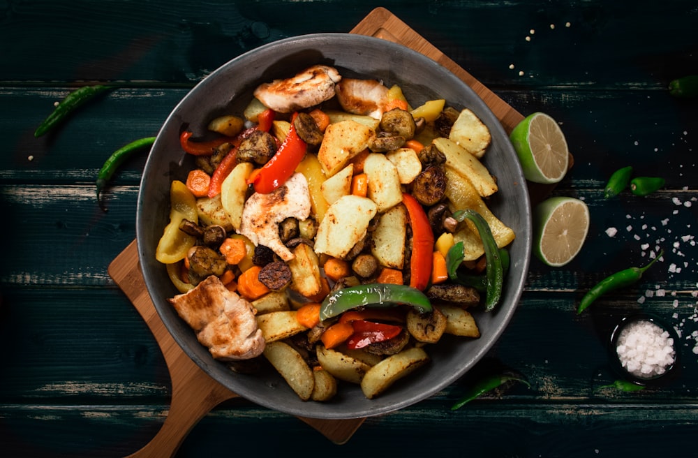 a pan filled with meat and vegetables on top of a wooden cutting board