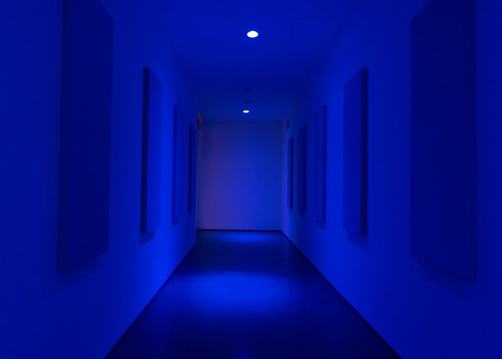 a dark hallway with blue lighting and a white wall