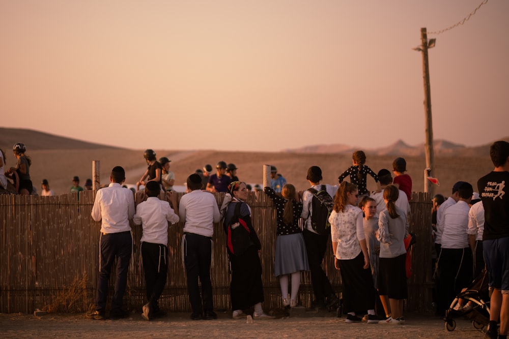 a group of people standing next to a wooden fence