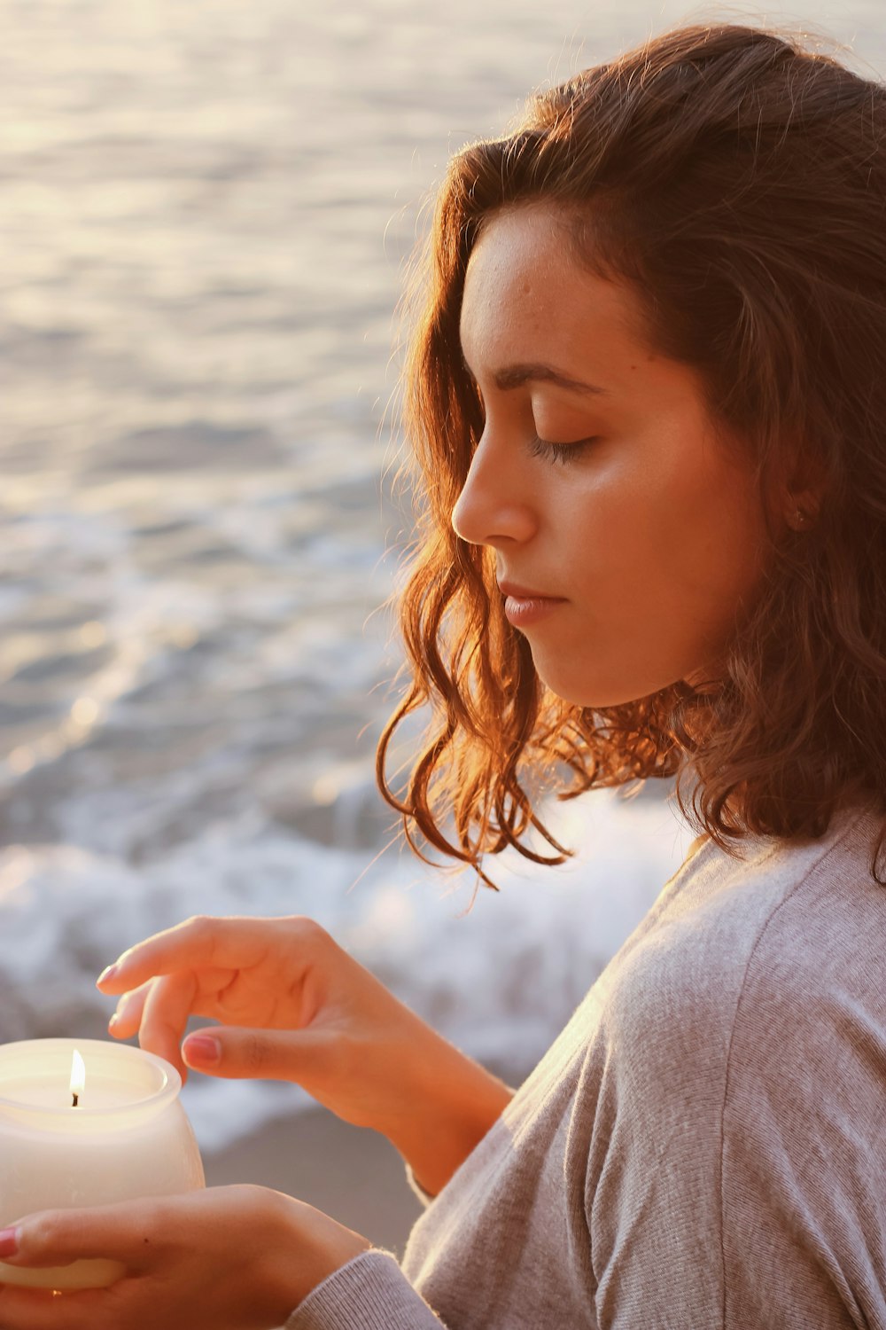 a woman holding a lit candle near the ocean