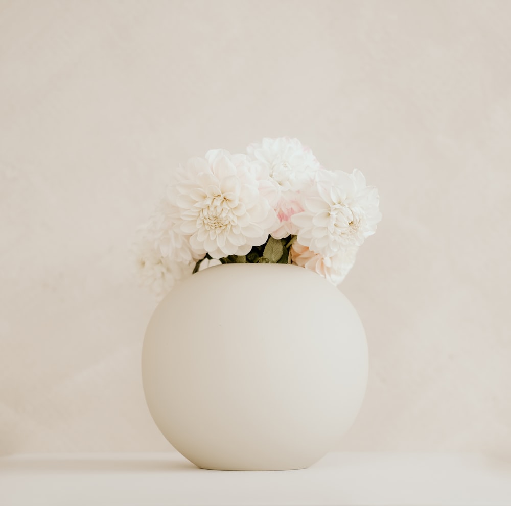 a white vase filled with white flowers on top of a table