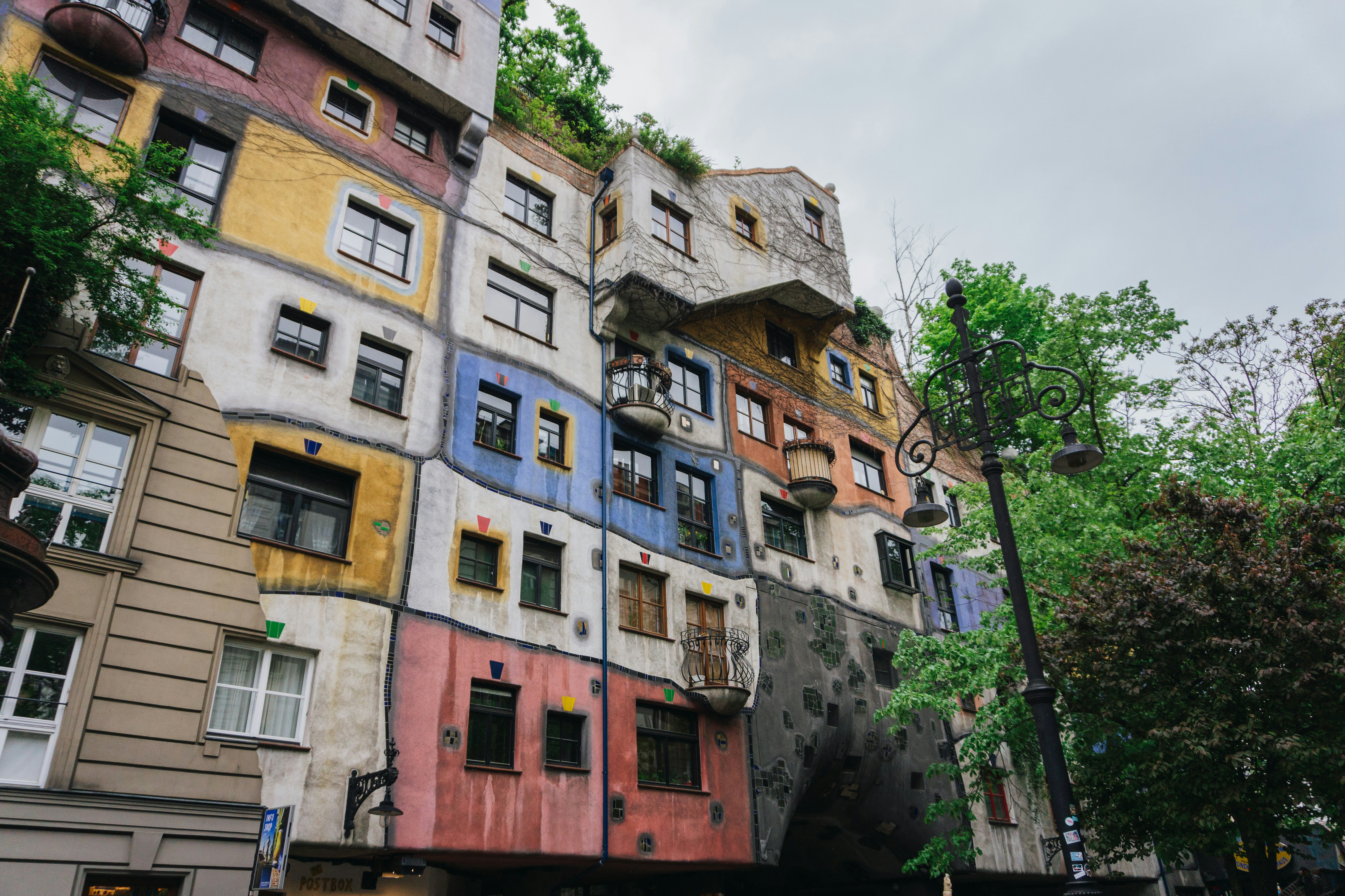Red tram in front of the iconic Hundertwasserhaus in Vienna, showcasing eclectic architecture and autumn foliage.