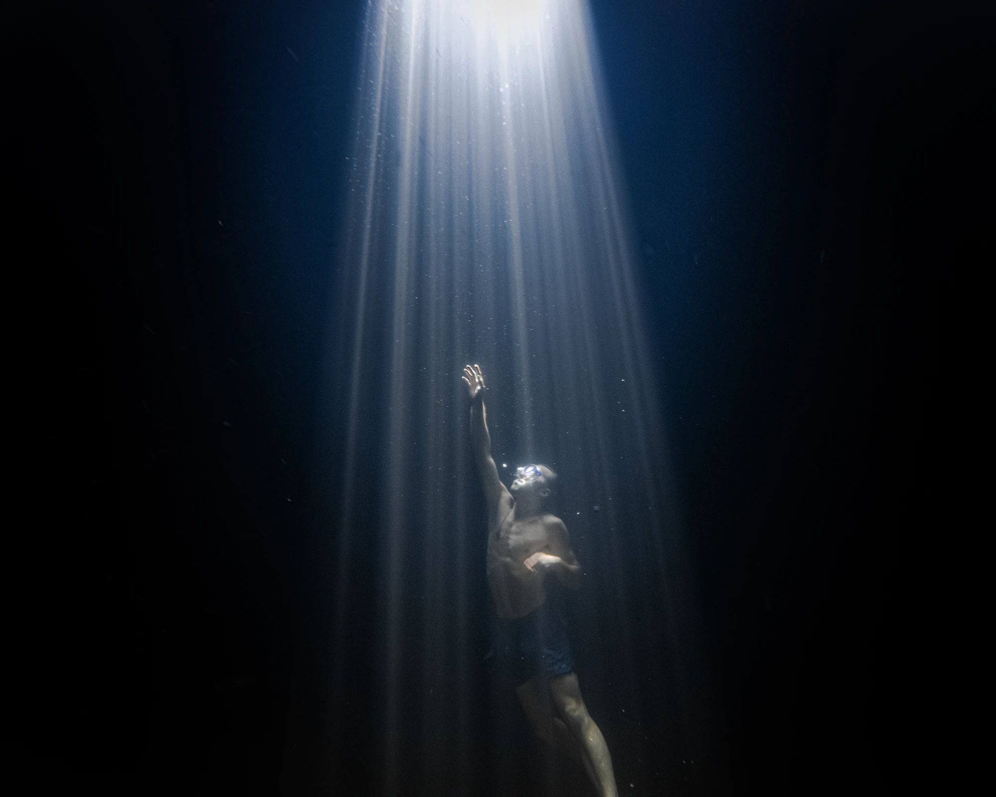 A person underwater reaching up toward light rays breaking the surface