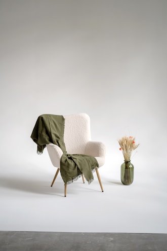 A soft linen throw draped over a modern armchair beside a minimalist lamp.