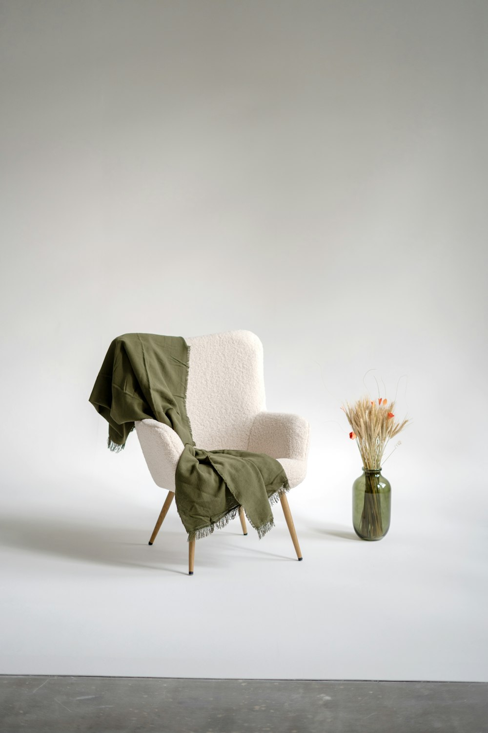 a chair with a blanket on it next to a vase with flowers