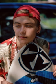 a young man holding a surfboard next to a car