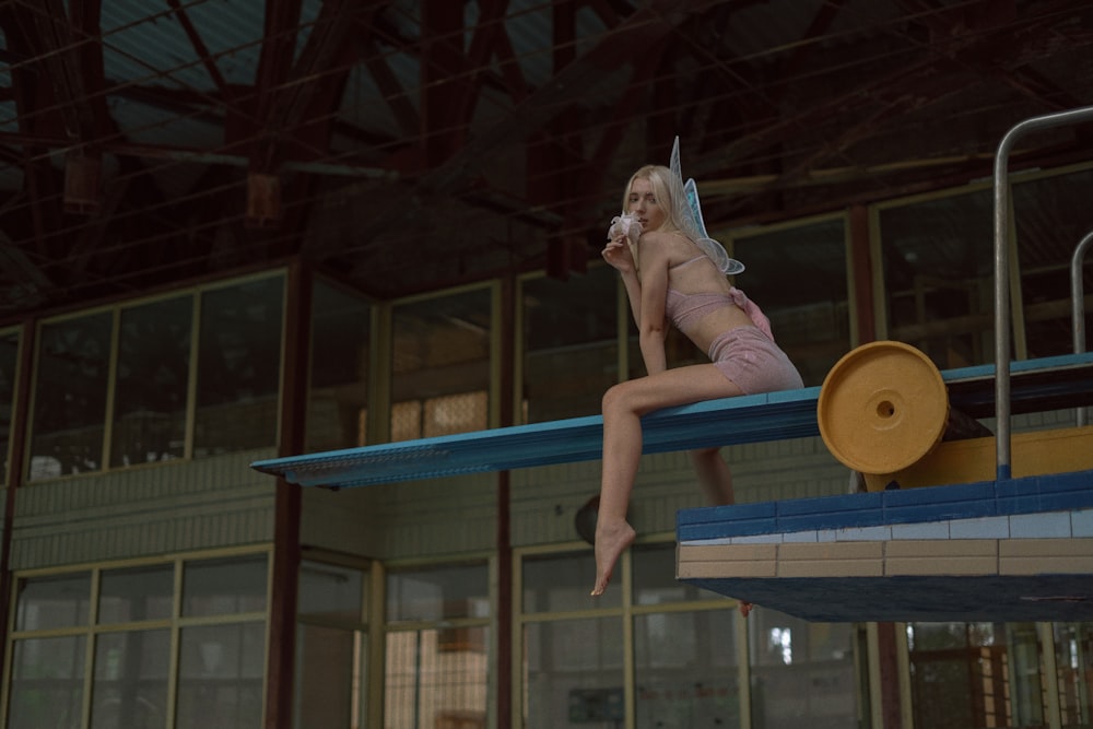 a woman in a bathing suit is sitting on a diving board