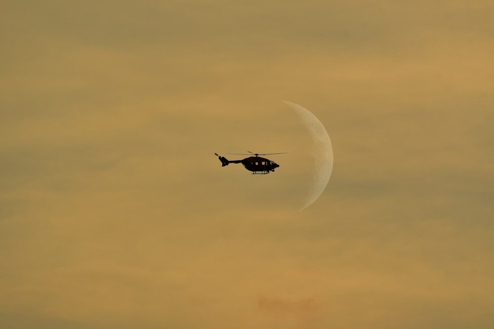 a helicopter flying in the sky with a half moon in the background