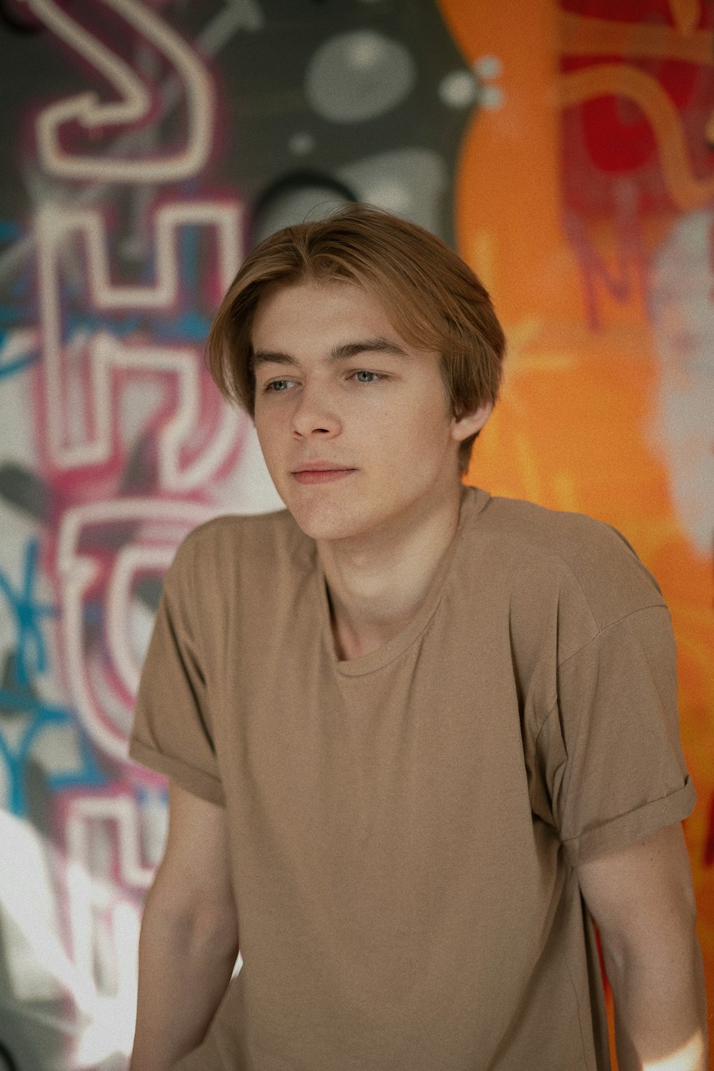 a young man sitting in front of a graffiti covered wall