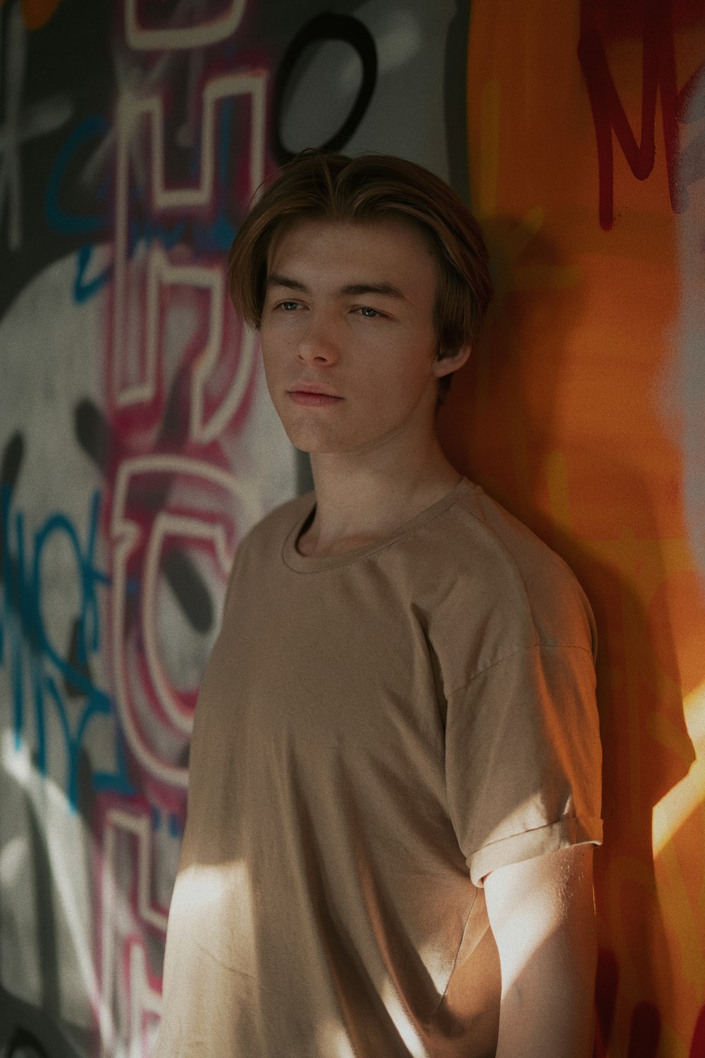 a young man standing in front of a graffiti covered wall