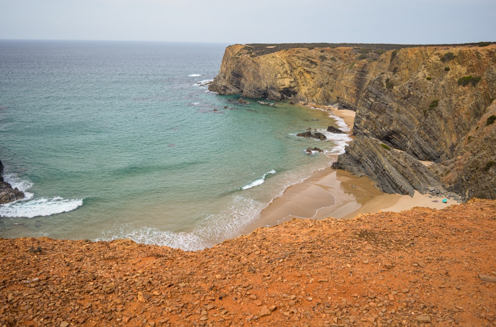 a sandy beach next to a cliff with a body of water