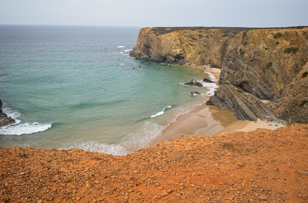 uma praia de areia ao lado de um penhasco com um corpo de água