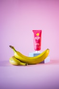 a banana and a tube of sunscreen on a pink background