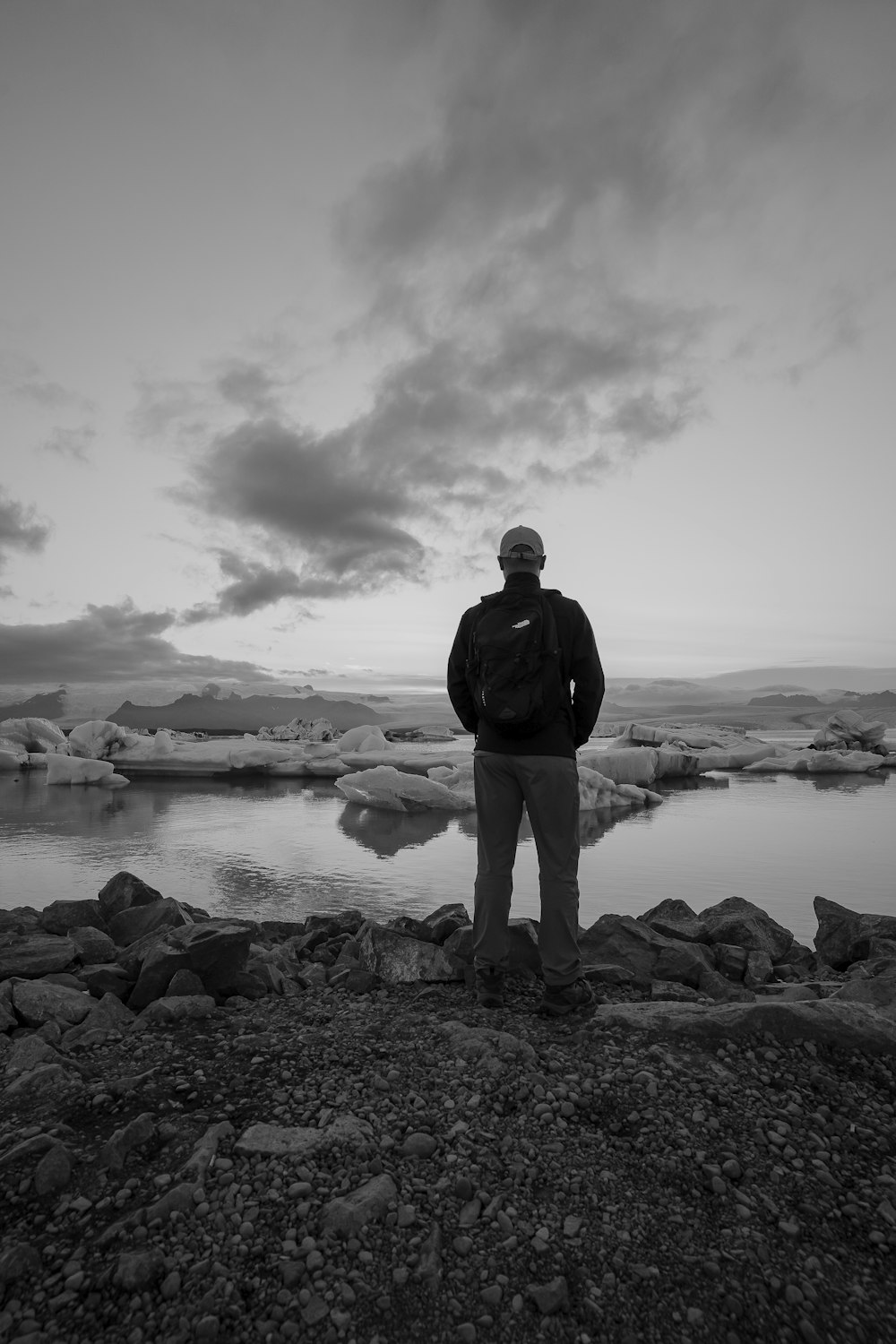 a man standing on a rocky beach next to a body of water