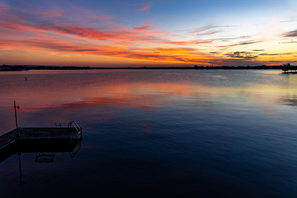 a boat floating on top of a lake under a colorful sky