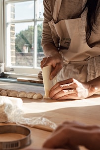 A baker carefully shaping dough in a clean, bright bakery kitchen.