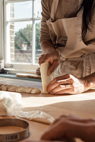 A smiling young woman in a floral apron baking bread, flour dusting the air in a sunlit kitchen.