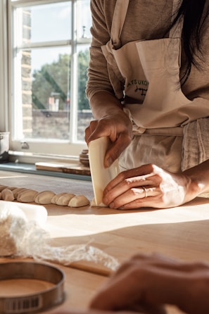 A baker shaping dough in a bright kitchen.