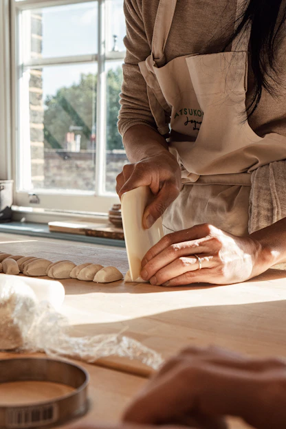 A baker gently shaping dough on a wooden countertop bathed in warm morning light.