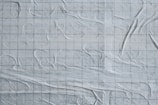 The image features a textured white surface with an overlay of faint grid lines. The surface appears to have a slightly wrinkled or crumpled appearance, giving it a dynamic, tactile feel.