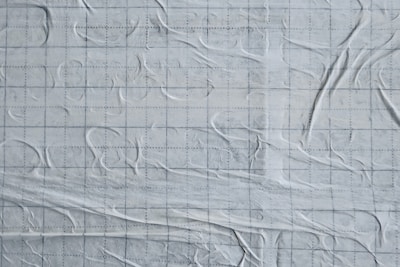 The image features a textured white surface with an overlay of faint grid lines. The surface appears to have a slightly wrinkled or crumpled appearance, giving it a dynamic, tactile feel.