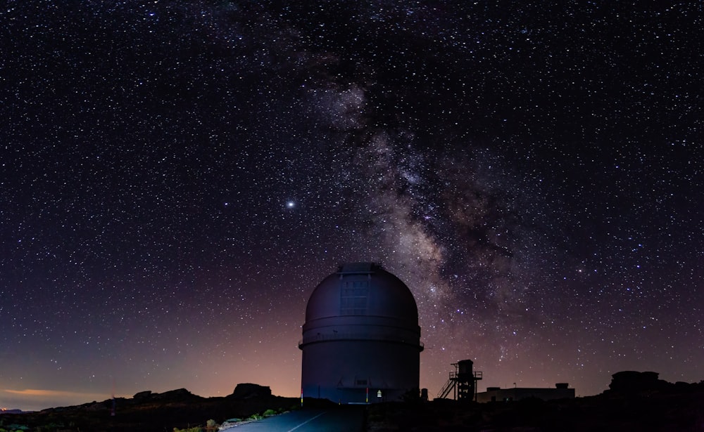 a large telescope on top of a hill under a night sky filled with stars