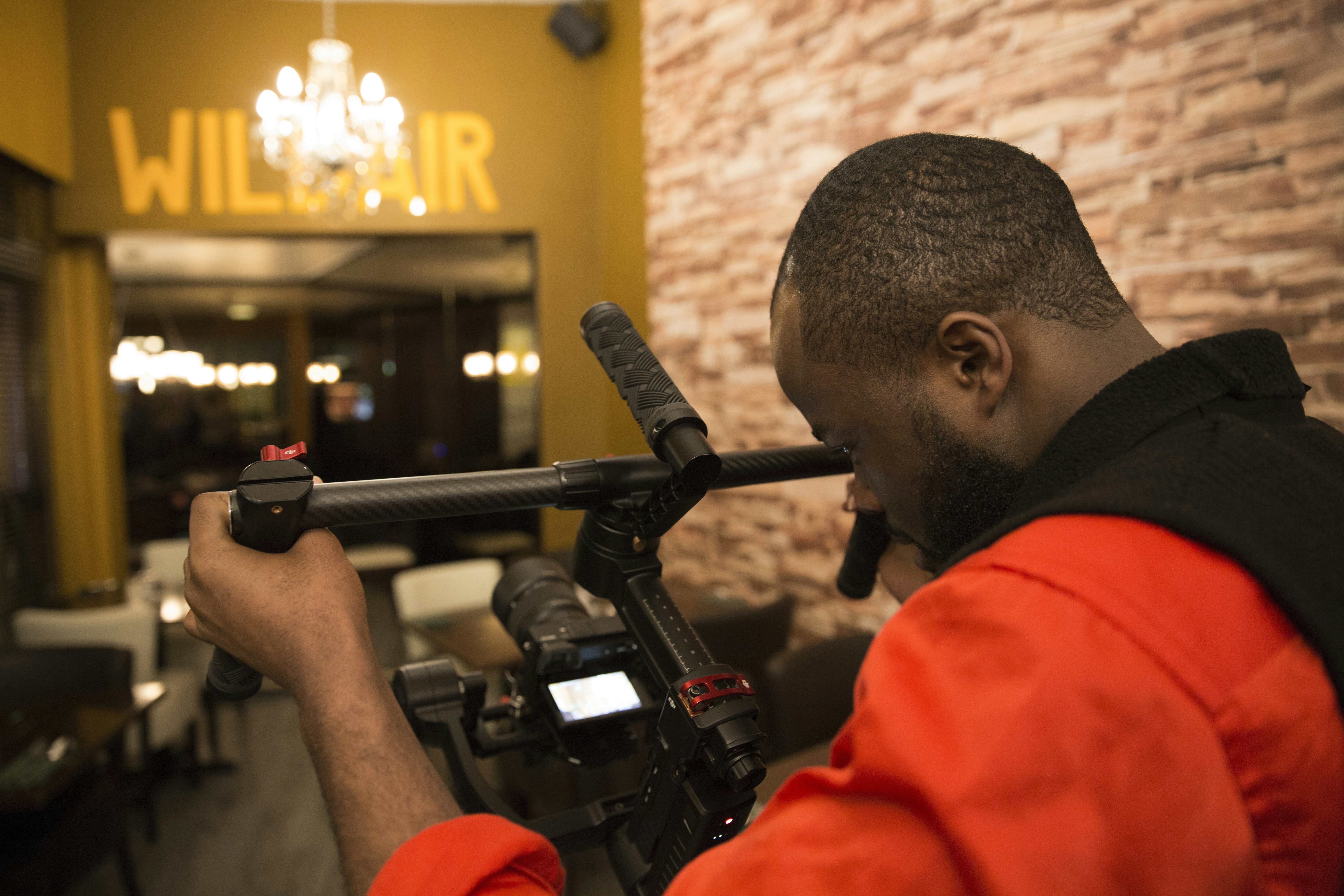 a man holding a video camera in front of a brick wall