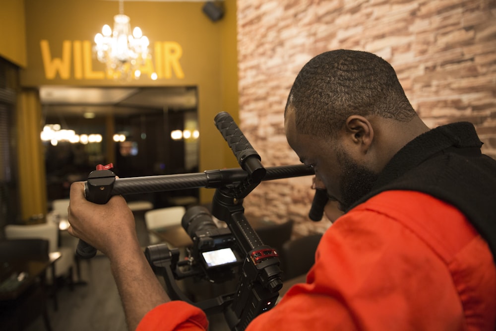 a man holding a video camera in front of a brick wall