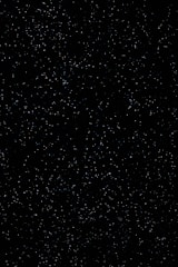 A vast expanse of a night sky filled with numerous small, white stars scattered across a dark black background, evoking a sense of infinite space.