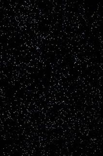 A vast expanse of a night sky filled with numerous small, white stars scattered across a dark black background, evoking a sense of infinite space.
