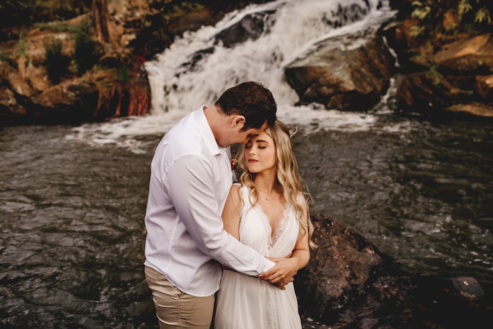 a man and a woman standing in front of a waterfall