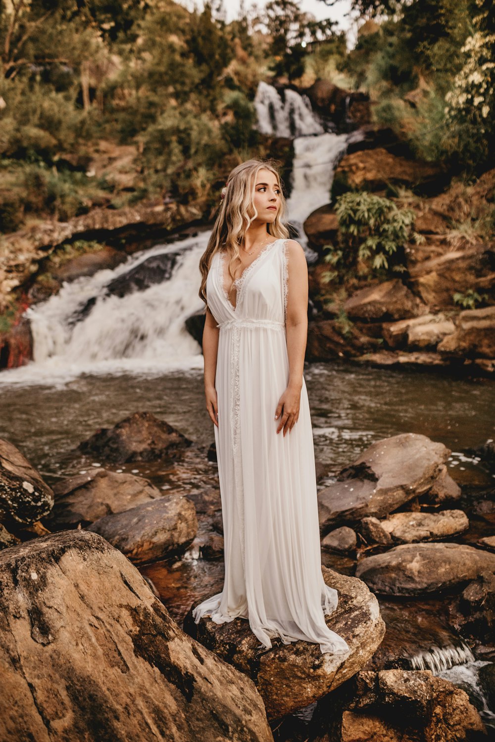 a woman standing on a rock in front of a waterfall